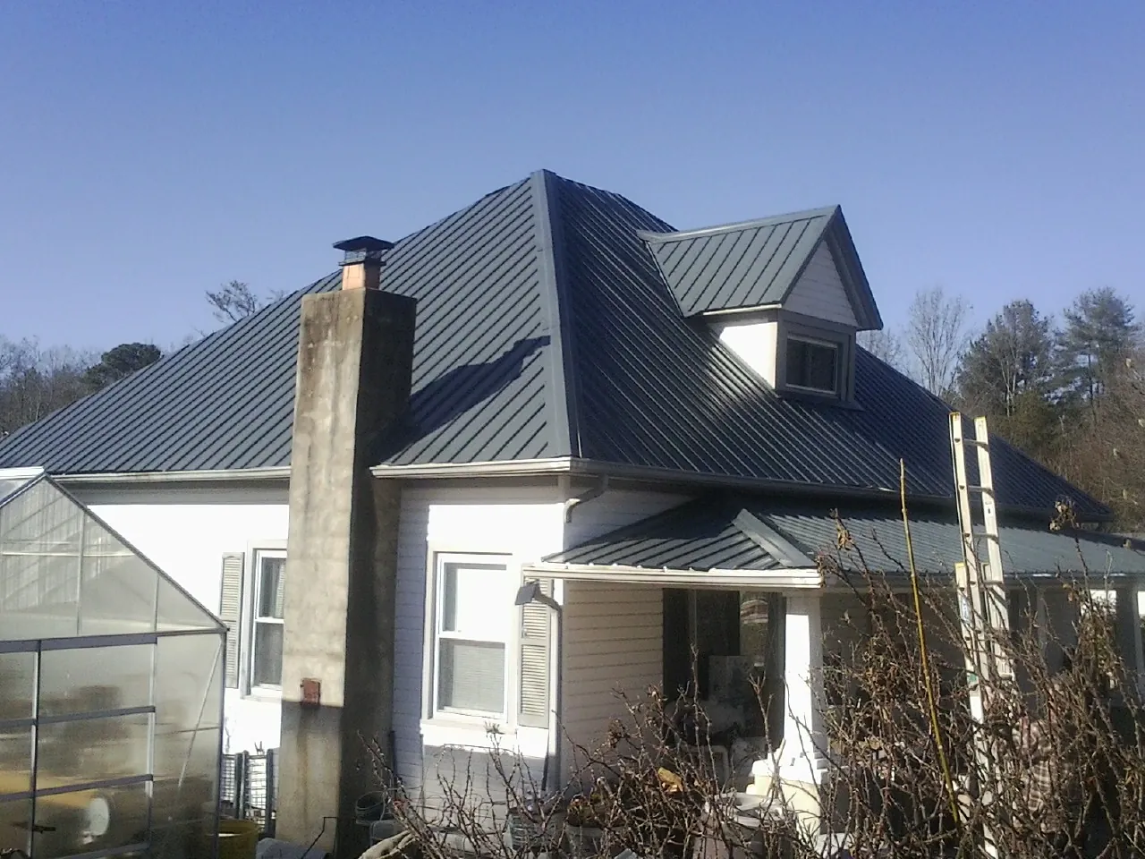 Dark blue standing seam metal roof on a white farmhouse with dormer — Slate & Tile Roof Repair by Roofing Brothers in Saline