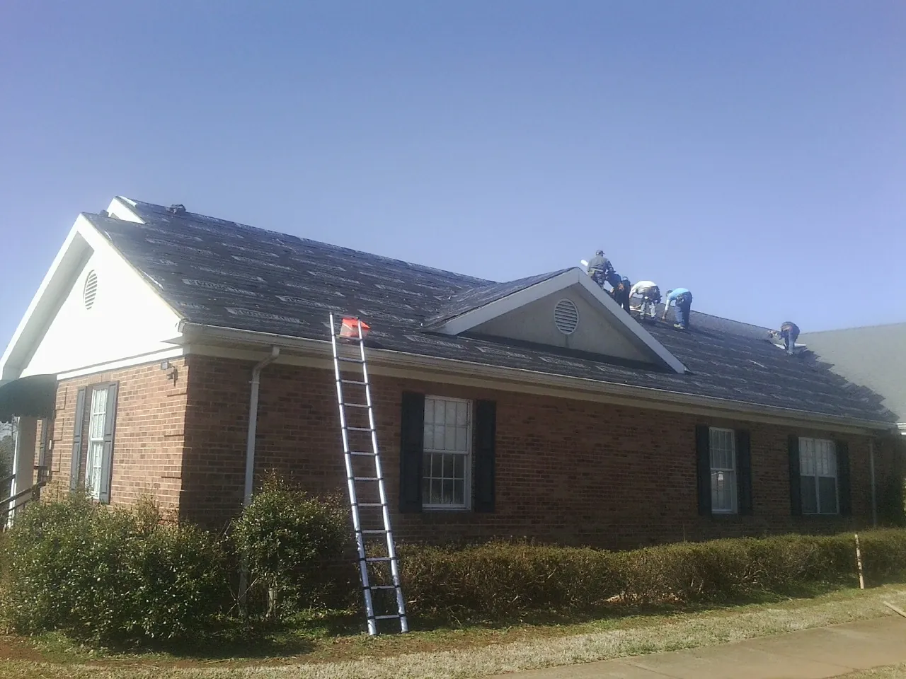 Crew tearing shingles off a brick ranch roof with a ladder set — Emergency Roof Repair work by our crew in Saline