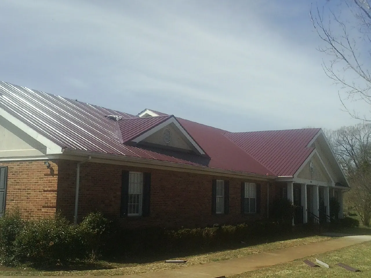 Red metal roof with gabled entries on a long brick building, from a Hail Damage Roof Repair job in Saline