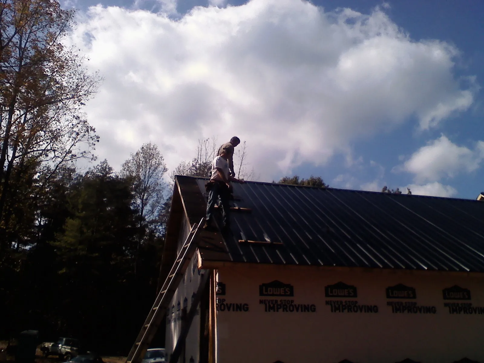 Roofer fastening dark metal panels high against a cloudy sky, from a Roof Inspection job in Saline